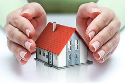 A model house on a table with someone’s hands either side, protecting it.