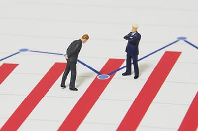 Two tiny model men in business suits on top of a printed graph.